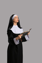 Young nun with Bible on grey background