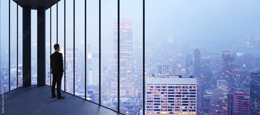 Poster businessman in empty office looking out of panoramic window with bright city downtown and sky view w