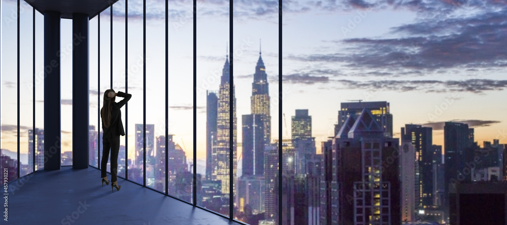 Poster female in suit standing in empty office looking out of panoramic window with bright city downtown an