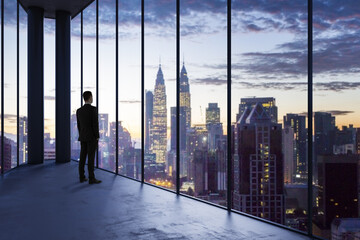 Business man in empty office looking out of panoramic window with bright city downtown view. Future, tomorrow, perspective and career concept.