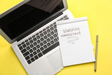 Notebook with text WORKPLACE HARASSMENT and laptop on color background