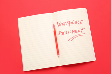 Notebook with text WORKPLACE HARASSMENT and pen on color background