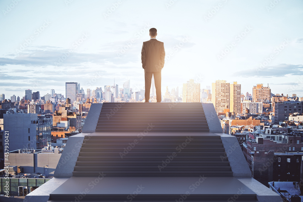 Poster Back view of young caucasian businessman standing on top of stairs on bright city background with sky view. Leadership, growth and success concept.