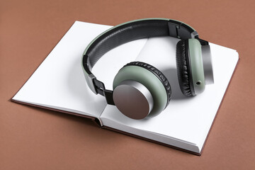 Modern headphones with book on color background