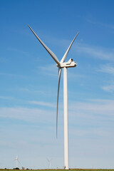 Windmill power generator in the foreground on a background with blue sky and other defocused mills