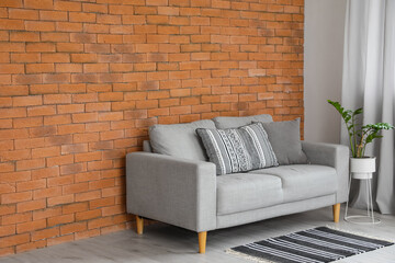 Naklejka premium Modern sofa and houseplant near brick wall