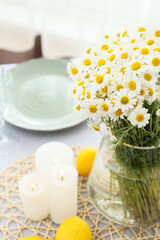 Vase with chamomile flowers, candles and lemons on table in room