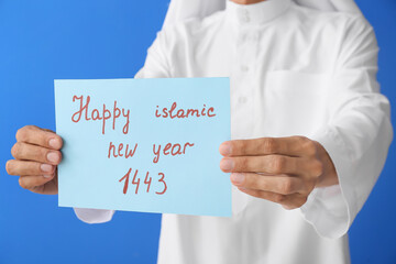 Young Muslim man with greeting card for Islamic New Year on color background, closeup