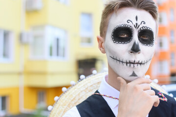 Young man with painted skull on his face outdoors. Celebration of Mexico's Day of the Dead (El Dia...
