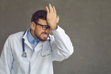 Damn idiot. Emotional male doctor smacks forehead as he remembers stupid mistake, foolish medical fiasco or professional failure at hospital, feeling dumb, annoyed and awkward, copy space background - obrazy, fototapety, plakaty