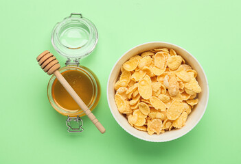 Bowl with tasty cornflakes and honey on color background