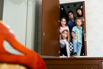 Surprised tween children peeking into quest room through open door in wall above dresser