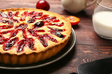 Plate with tasty plum pie and glass of milk on wooden background, closeup
