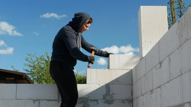 A young builder is building a house with his own hands. Bricklayer lays white brick blocks