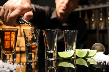 Bartender pouring tasty tequila into glasses at table in bar, closeup