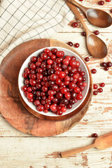 Bowl with healthy cranberry on light wooden background