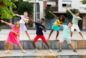 International group of modern tweenagers performing street dance choreography outdoors in summer..