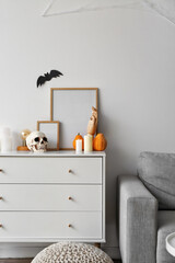 Blank frames with Halloween decorations on chest of drawers near light wall