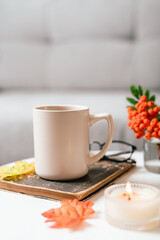 Still life book, candle, rowan berry and a cup of tea or coffee in the living room on a table, home decor in a cozy house. Autumn weekend concept, blanket and plaid. Fallen leaves and home decoration