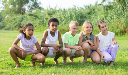 Multiracial group of cheerful preteen friends gaily spending time outdoors on sunny summer day,...