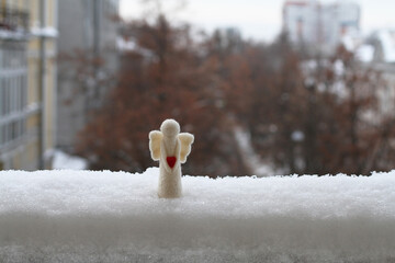 A woolen toy angel stands in the snow on the railing of the balcony against the street. Cloudy...