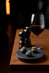Black seafood tartlets as an unusual appetizer in a seafood restaurant, served with a glass of red wine, side view