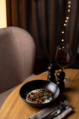 A portion of raw beef steak with blood and rich cream sauce on a round wooden table in a restaurant, no people