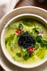 Close up, above view of fine dining green cold soup with a pile of black caviar and fresh flowers