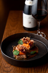 Gourmet salmon steaks with sour-sweet sauce and a bottle of red wine, side view, dark atmospheric restaurant