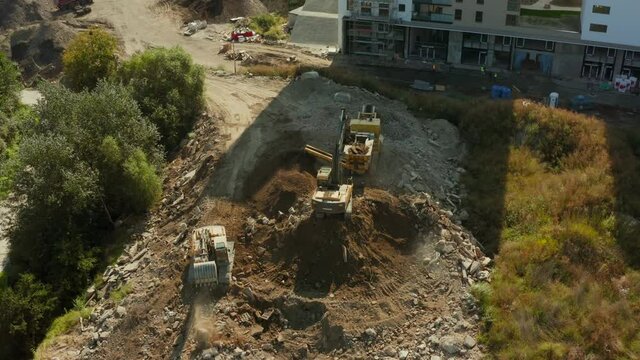 An aerial view of the excavator loading stones into the rock crusher. Two heavy excavators dig out large rocks and smash them into the ground and load them into a crusher to produce crushed rock 