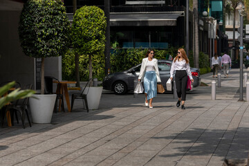dos mujeres cargando bolsas de  las compras que hicieron  mientras caminan platicando por la calle.