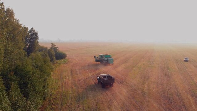A Combine harvester filled with grain drives through the cut field after harvest, followed by a grain truck. Drone douches agricultural fields, agro-industry harvesting wheat.