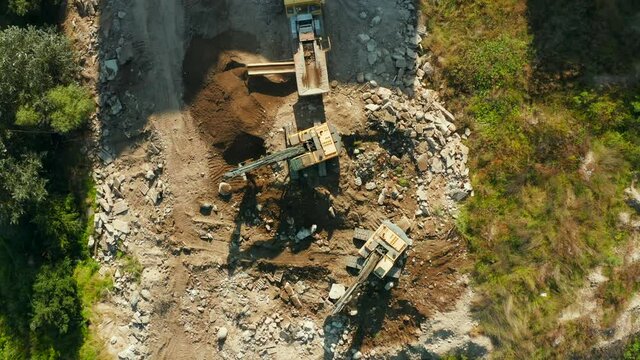 Top down view of Two Excavators digging the ground and breaking up large rocks and loading rock into a crushing plant to be processed into crushed rock.