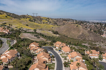 Aerial view of a suburban southern California community in the hills.  Sunny day with silky clouds, power lines visible
