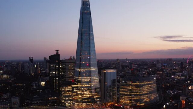 Tall modern glossy glass covered building towering above surroundings. Elevated aerial evening view against twilight sky. London, UK