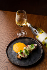 Chicken breast shish kebab with mango sauce on a black plate with a bottle of white wine