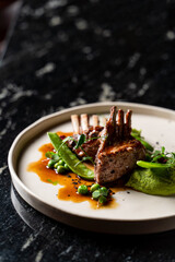 Top view of juicy roasted ribs with green puree and peas on black marble background