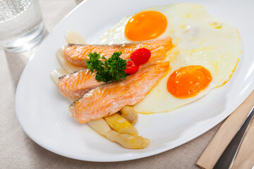 Delicious breakfast. Over easy fried eggs with salmon steaks and baked white asparagus