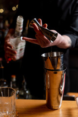 Bartender is making a cocktail in a dark bar of a restaurant, male hands only visible