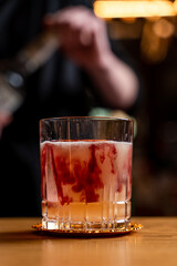 Beautiful swirls in a glass of alcoholic cocktail with yellow and red layers, close up on a wooden bar counter