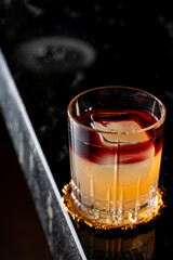 Layered alcoholic cocktail in a black marble bar counter with a reflection on it
