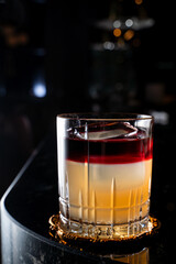 Layered alcoholic cocktail in a black marble bar counter with a reflection on it