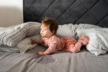 Small caucasian baby lying down on the belly on the bed with wet urine stain on the sheet and clothes looking to the side Bedwetting child pee on the bed - obrazy, fototapety, plakaty