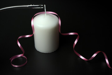 Obraz premium I light a large white candle with a pink ribbon on a black background.