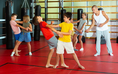 Fototapeta na wymiar Preteen children practicing in pair self-defence movements with male trainer supervision