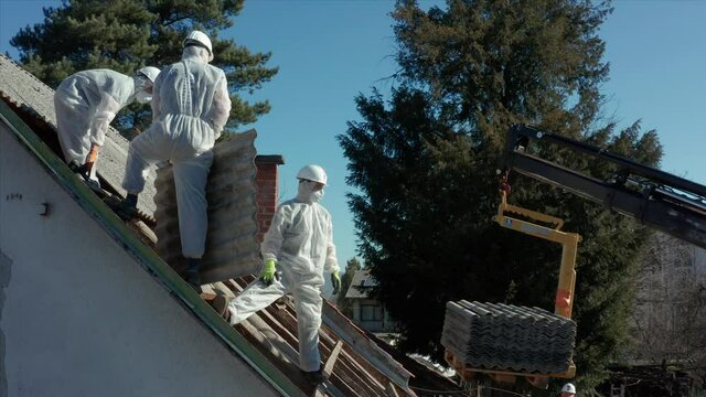 Aerial shot circling around roofers in hazmat suits to remove Asbestos during a renovation.