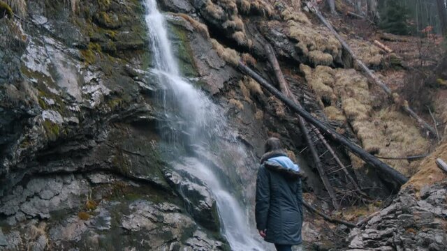 Girl marvels on the beauty of a waterfall with a basin in Switzerland.