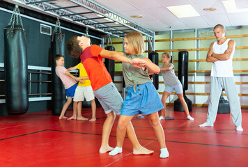 Fototapeta na wymiar Positive kids in pair exercising self-defense movements during group class with male coach