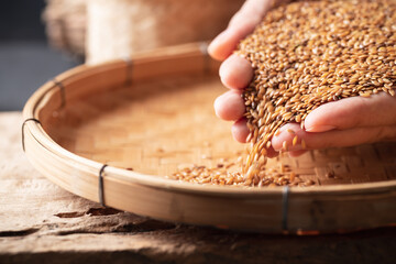 Brown flax seed holding by hand and pouring on bamboo tray