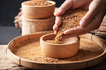 Brown flax seed holding by hand and pouring in a bowl on bamboo tray